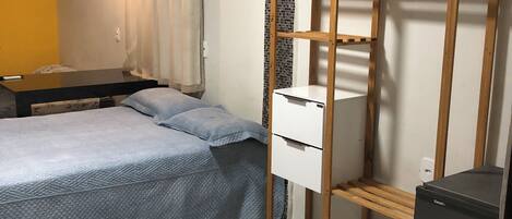 Un dormitorio con cama, armario, escritorio pequeño y refrigerador.