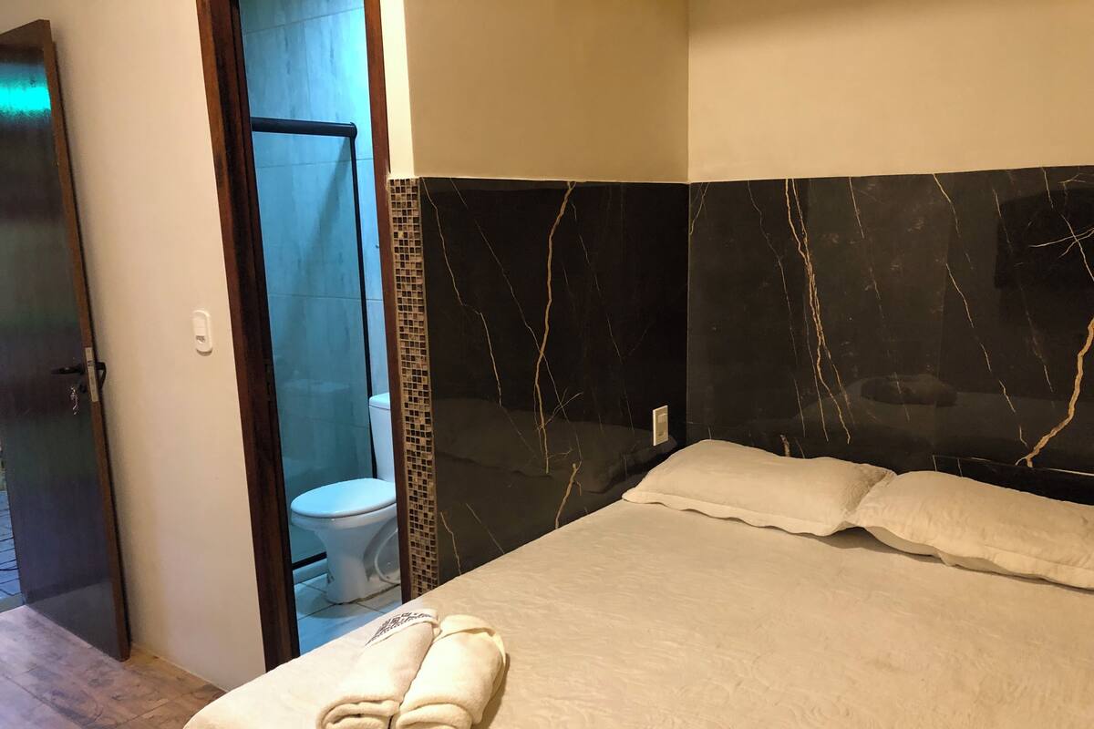A hotel room with a bed, a bathroom, and a door leading to another room.