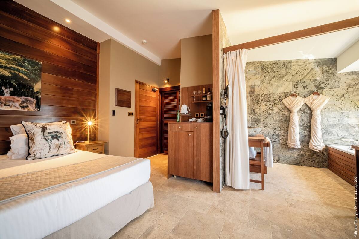 A bedroom with a bed, wooden paneling, a nightstand, a wardrobe, a bathroom with a shower, and a towel rack.