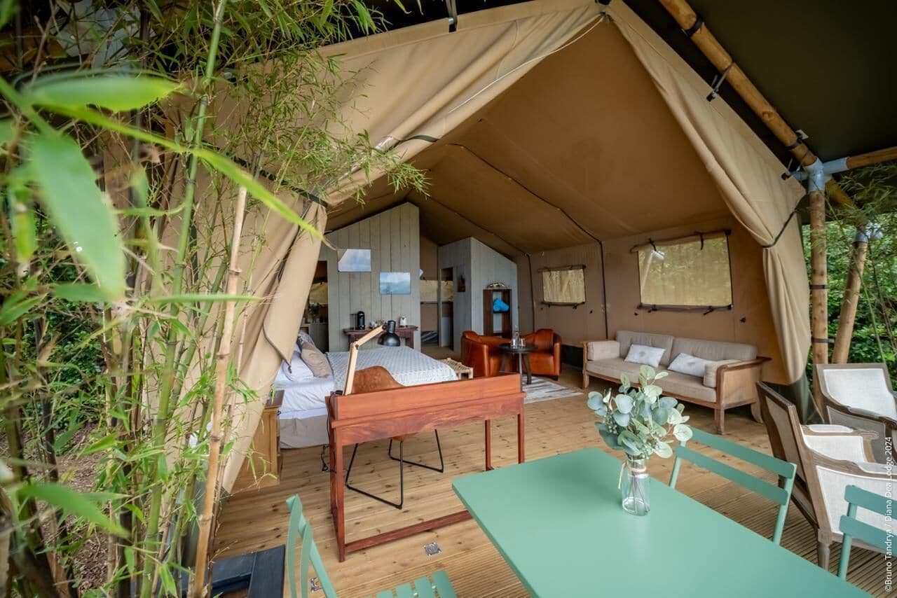 A tented accommodation with a wooden bed, a sofa, and a dining table.