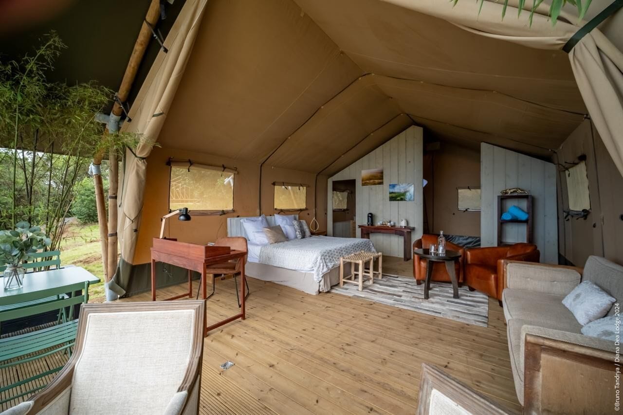 A tented accommodation with a bed, seating area, and a small table.