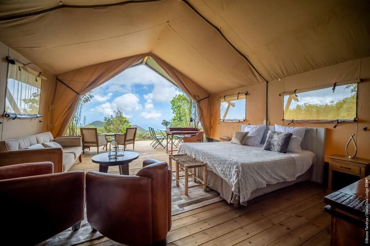 A tented accommodation with a bed, seating area, and a table.