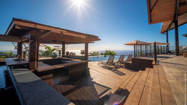 Um deck de madeira com piscina, cadeiras de descanso e vista para o oceano.
