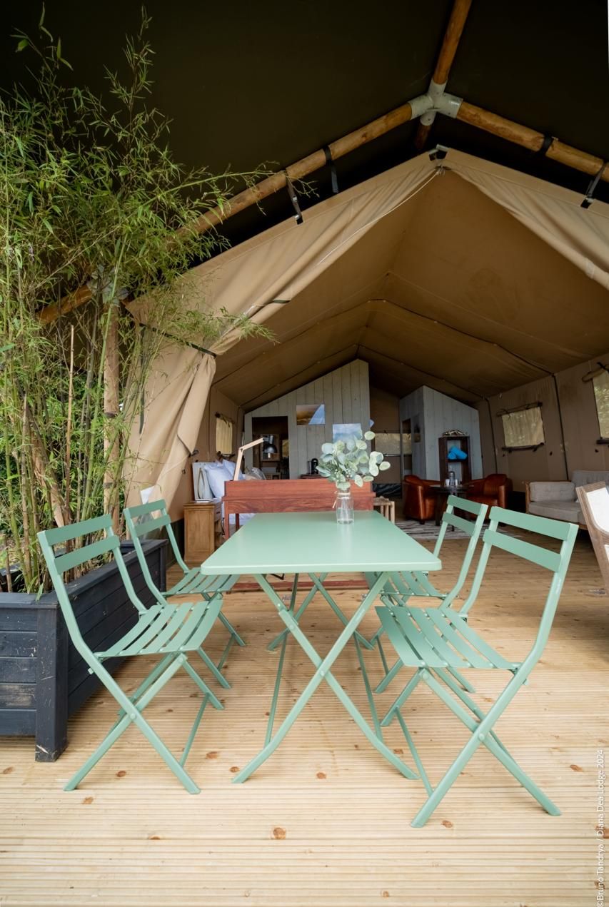 A tented accommodation with a dining area featuring a table and chairs, surrounded by bamboo plants.