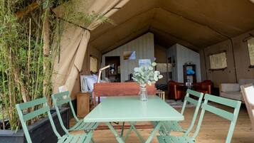 Alojamiento en carpa con zona de comedor que incluye una mesa y sillas, rodeado de plantas de bambú.
