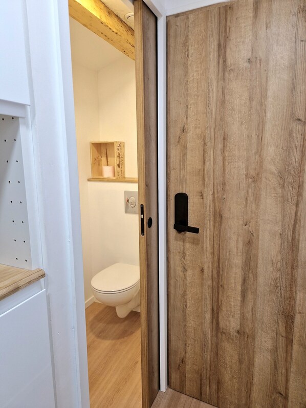 Une porte en bois avec une poignée noire, un mur blanc et une étagère en bois sur laquelle repose une bobine de fil.