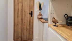 Un corridoio con una porta in legno, un piccolo ripiano con oggetti decorativi e una statuina di uccello.