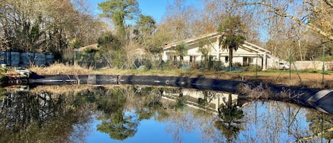 A house with a pond in front, surrounded by trees and a fence.