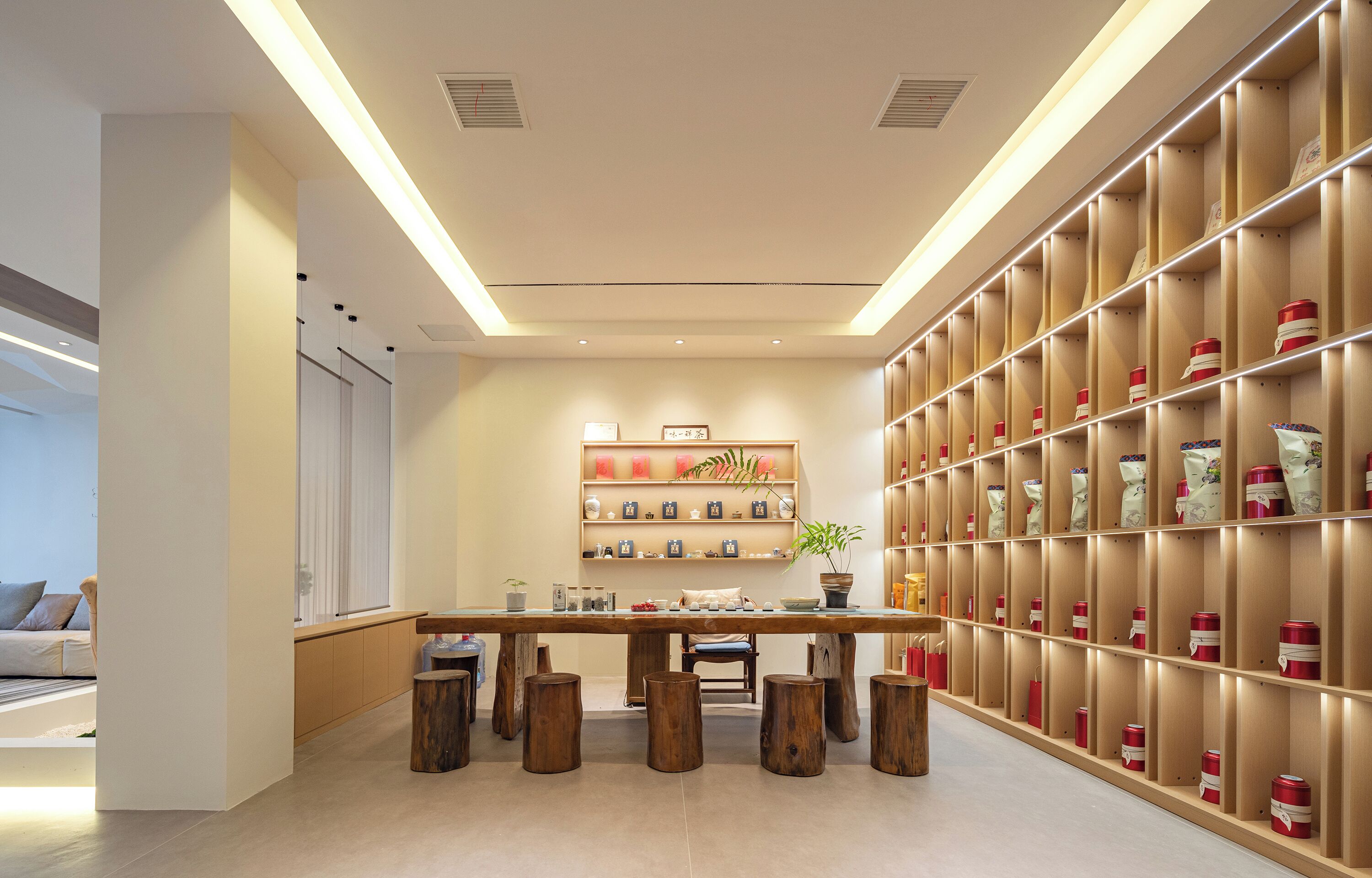 A modern interior with a wooden table and stools, a bookshelf with decorative items, and a large wall of storage bins.