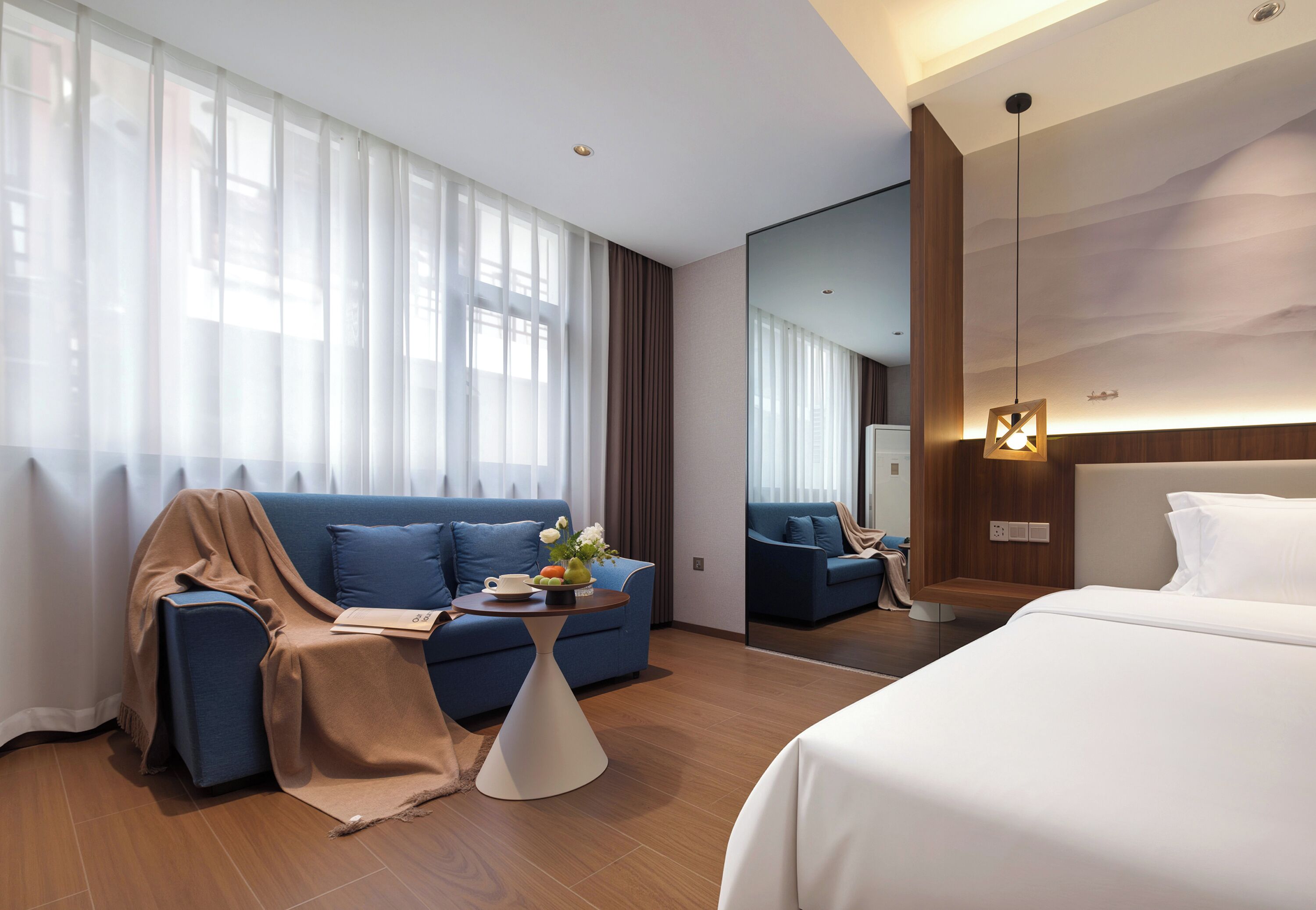 Ein modernes Hotelzimmer mit einem großen Bett, einer Couch, einem kleinen Tisch mit Blumen und einem großen Spiegel.