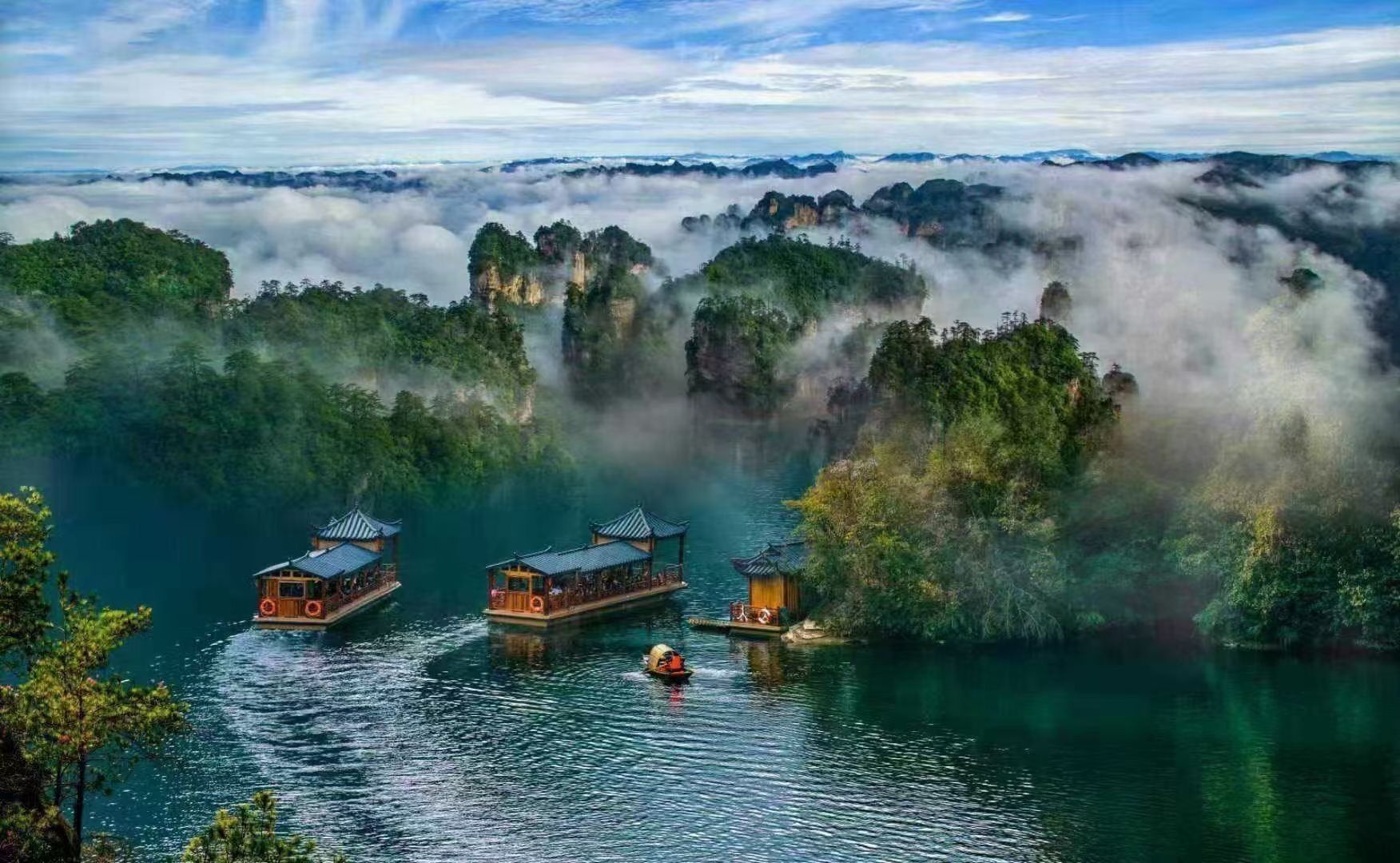 A serene lakeside scene with traditional wooden boats and a small pavilion, surrounded by lush greenery and mist-covered cliffs.