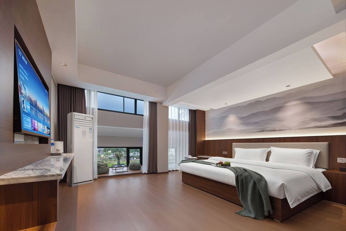 Ein modernes Hotelzimmer mit einem großen Bett, einem Flachbildfernseher und Blick ins Freie.