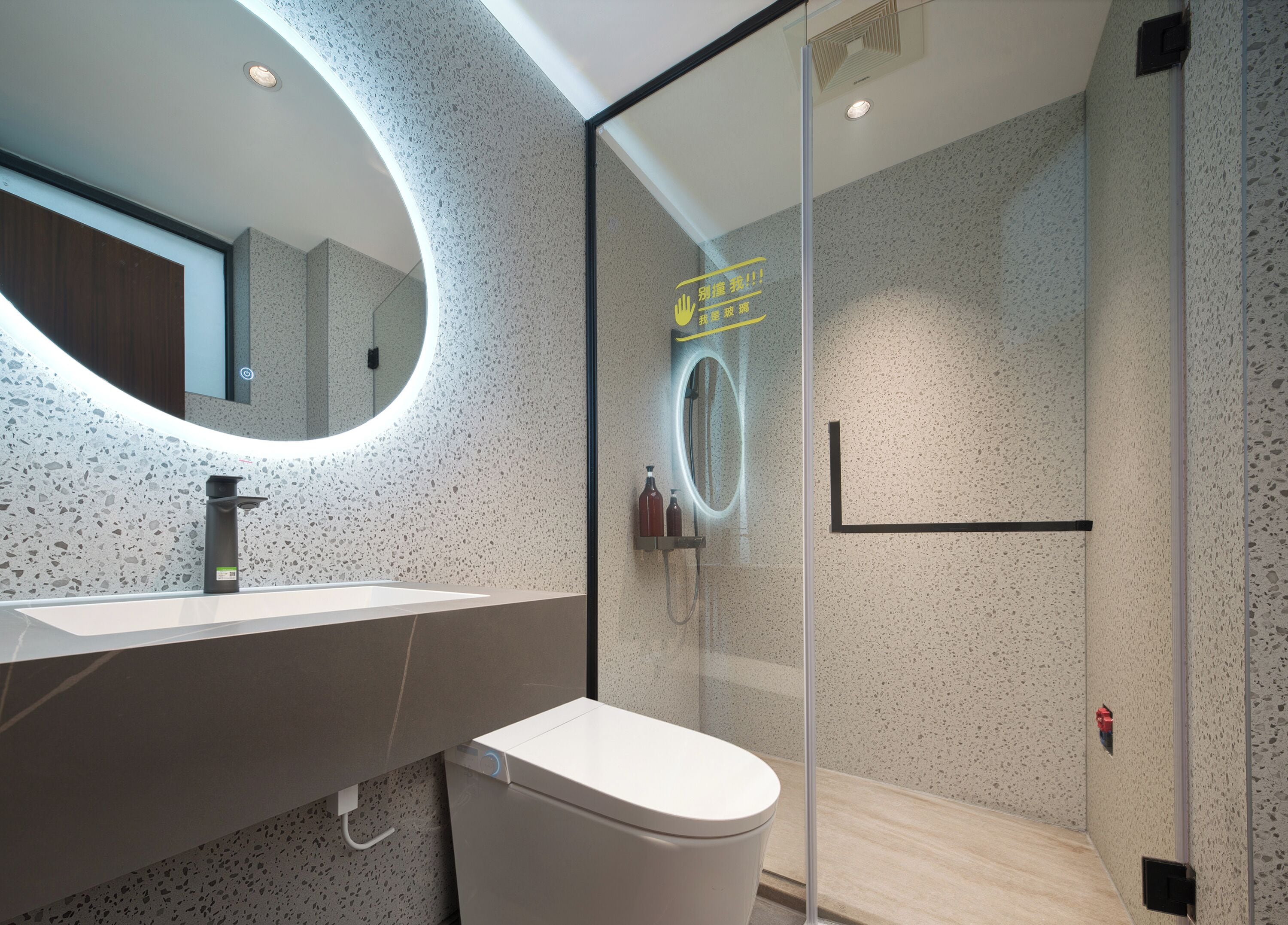 Un baño moderno con un espejo redondo, un inodoro y una zona de ducha con mampara de vidrio.