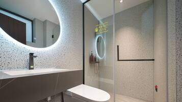Un baño moderno con un espejo redondo, un inodoro y una zona de ducha con mampara de vidrio.