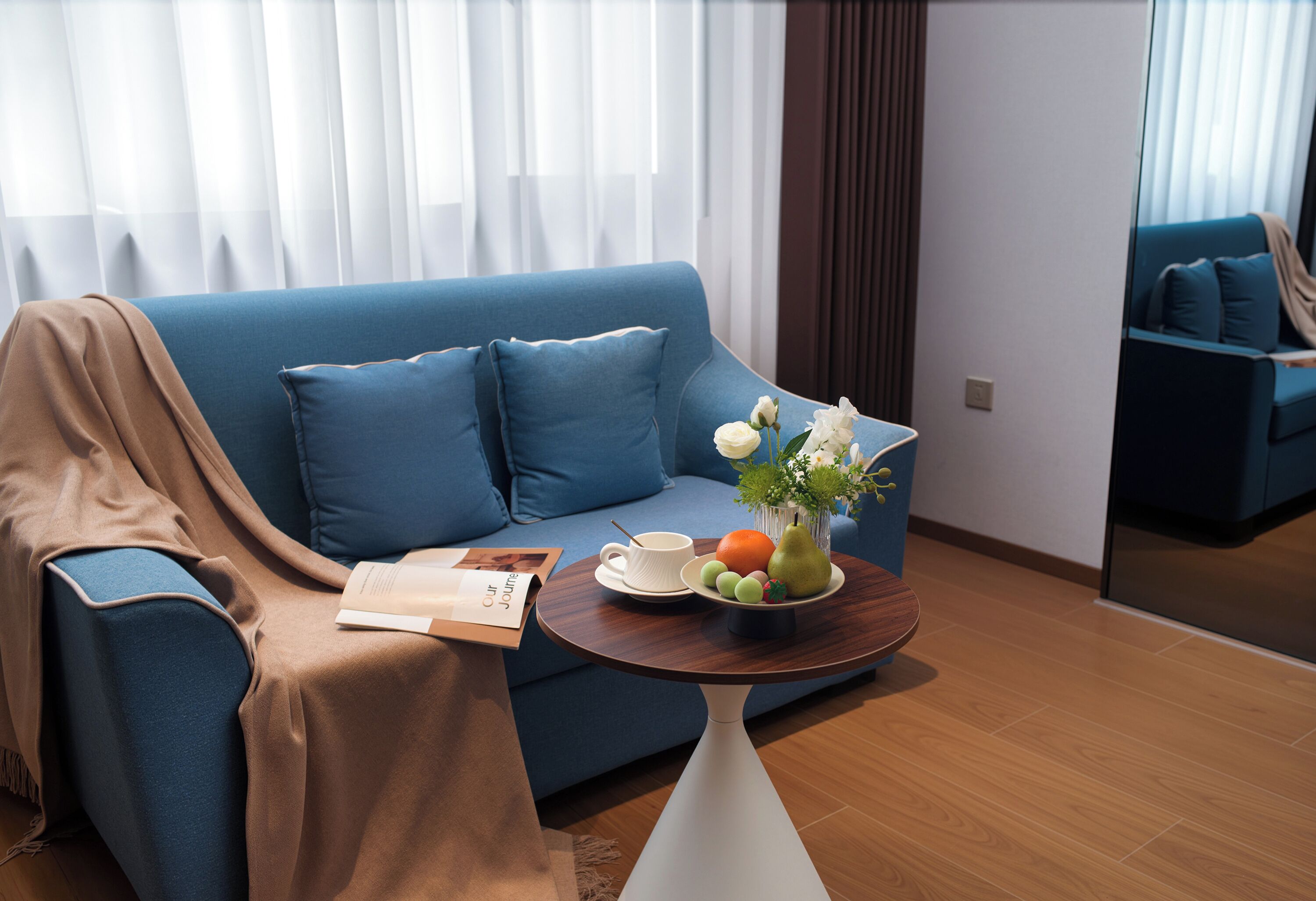 Ein modernes Wohnzimmer mit einem blauen Sofa, einem Couchtisch mit Früchten und Blumen sowie einer Zeitschrift auf dem Sofa.