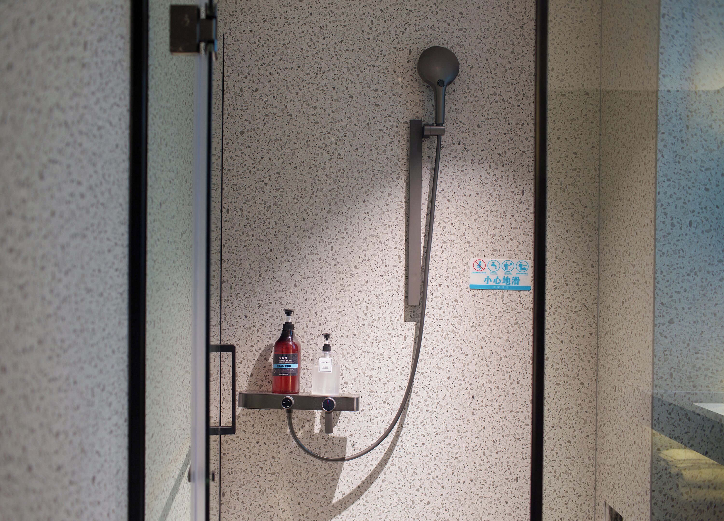 A shower with a handheld showerhead, a soap dispenser, and a shampoo bottle.