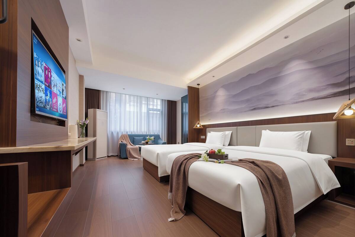 Ein Hotelzimmer mit zwei Betten, einem Fernseher, einem Schreibtisch und einem großen Fenster.