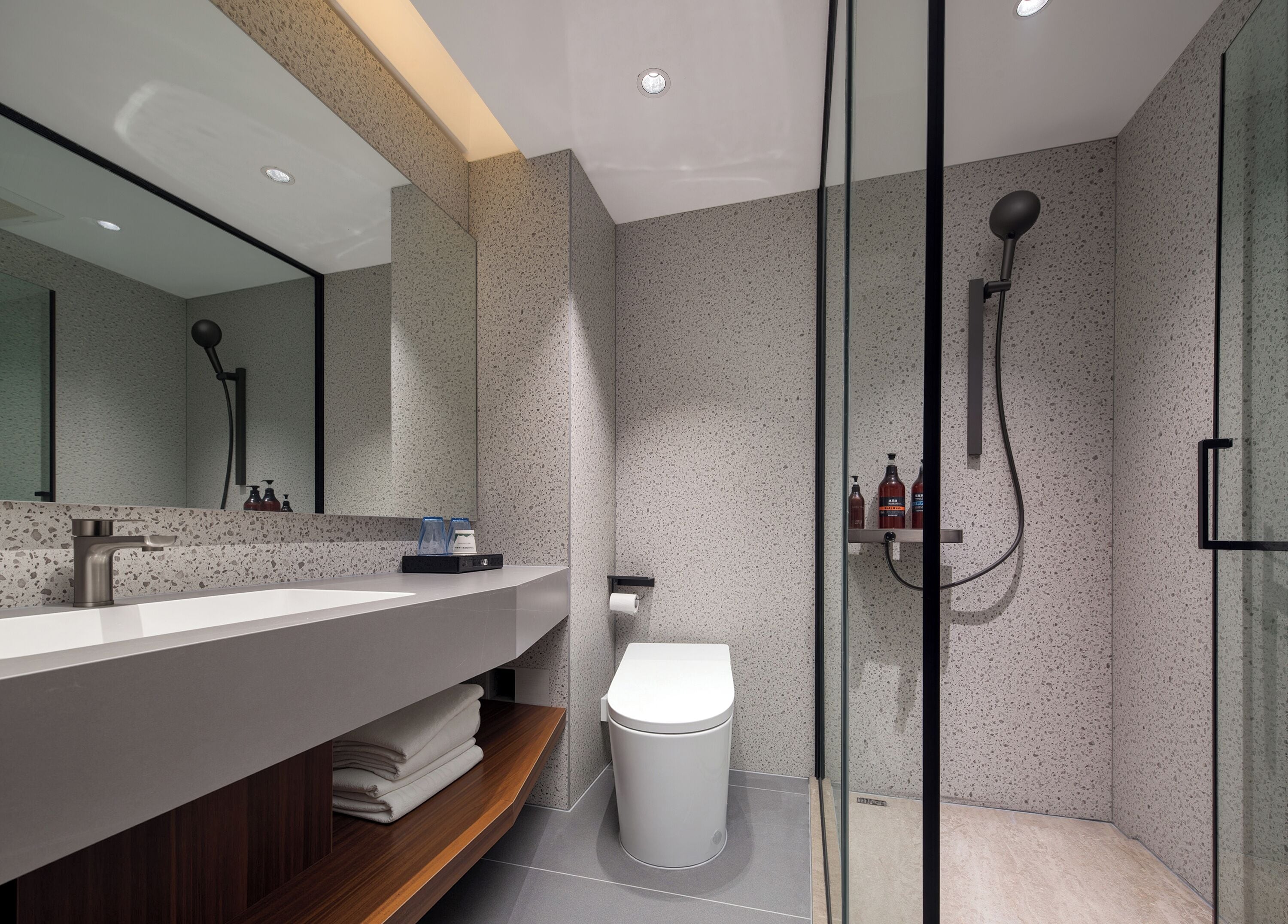 Un baño moderno con cabina de ducha de vidrio, inodoro blanco y tocador con espejo.