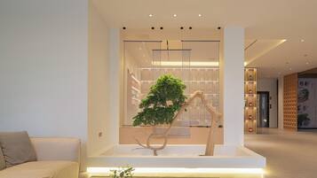 Un interno moderno con un design minimalista, caratterizzato da una scultura arborea al centro, un divano e un'area reception con parete e scaffali in legno.