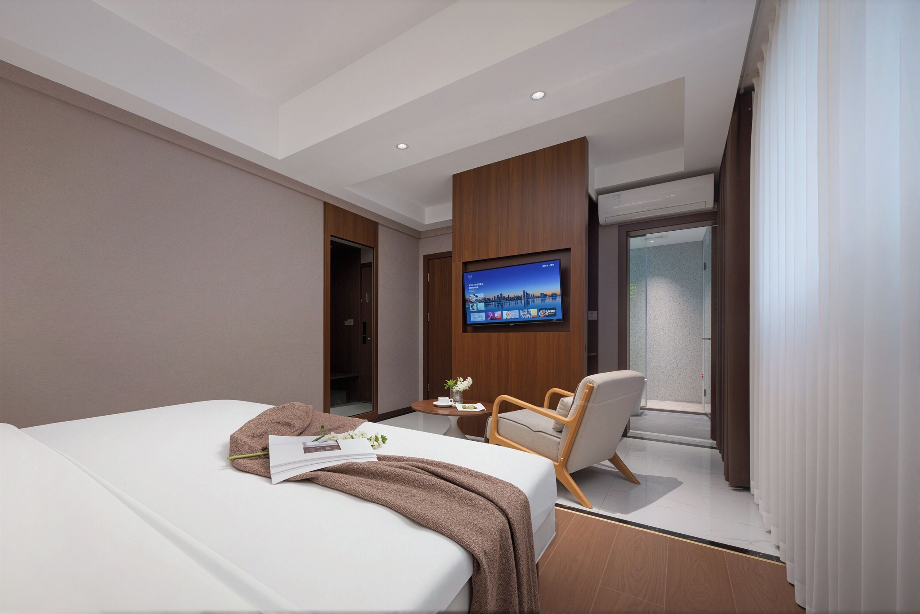 Habitación de hotel moderna con una cama grande, un televisor montado en la pared, una mesita con una planta y una ventana con cortinas.