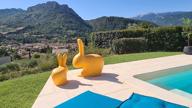 A pool area with two yellow chairs, a potted plant, and a view of a town and mountains in the background. - In a postcard setting! Villa 10 people Drome Provençale  (Buis-les-Baronnies)