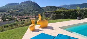 A pool area with two yellow chairs, a potted plant, and a view of a town and mountains in the background.