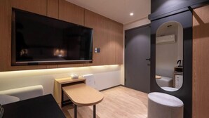 A modern hotel room with a large flat-screen TV mounted on the wall, a small desk with a chair, a round mirror, and a compact toilet. - Songdo Stay Sotam (Incheon)