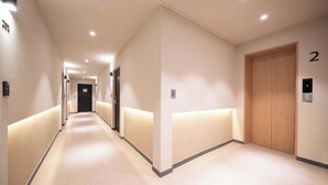 A modern hotel corridor with a carpeted floor, recessed lighting, and a wooden door marked with the number 2. - Songdo Stay Sotam (Incheon)