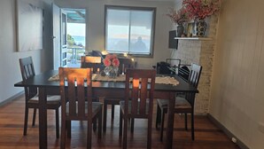 A dining area with a wooden table and chairs, a vase of flowers, and a view of the ocean through a large window.