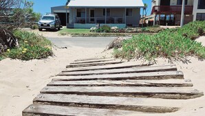 A wooden staircase leading to a building with a white roof, surrounded by sparse vegetation and a clear sky.