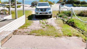 A white Nissan car parked under a covered area with a view of the beach and ocean.