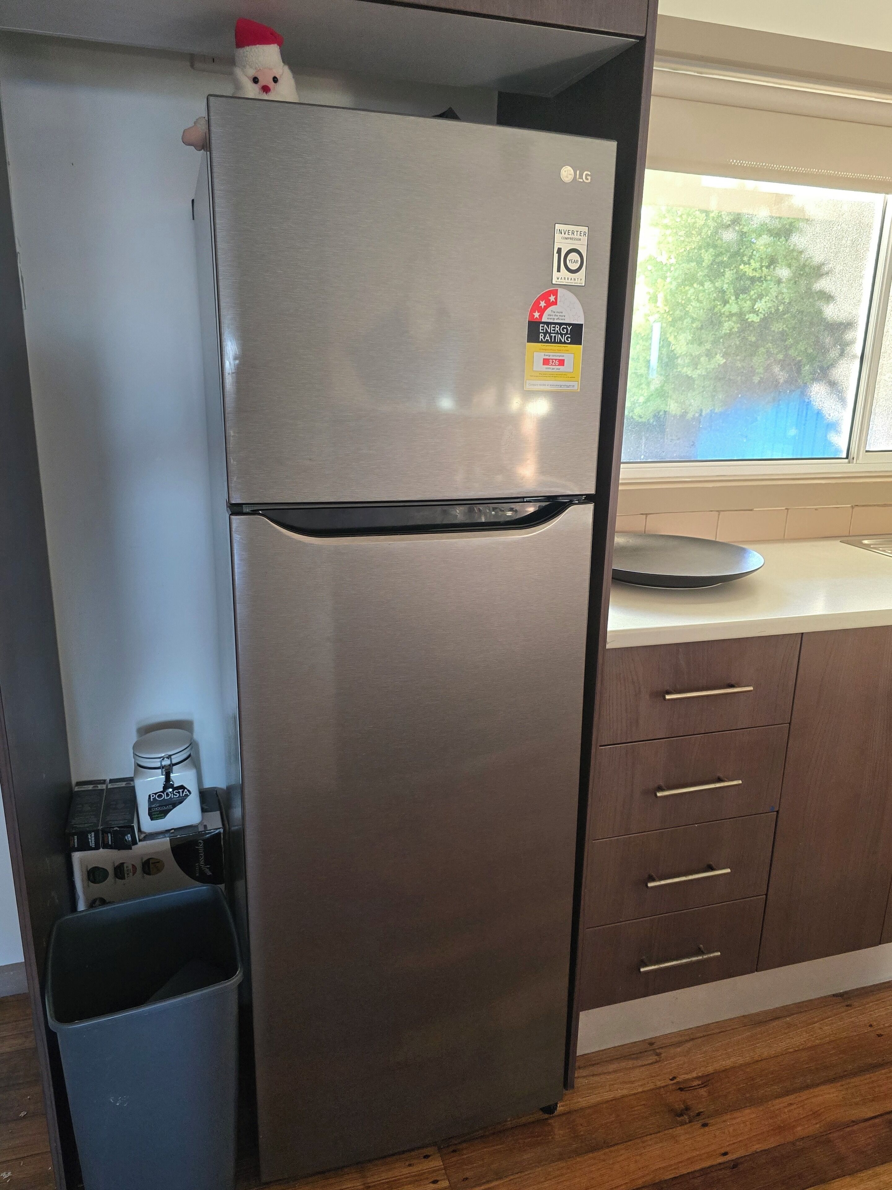 A stainless steel refrigerator with an ENERGY STAR rating sticker, a small trash bin, and a coffee maker on the lower shelf.