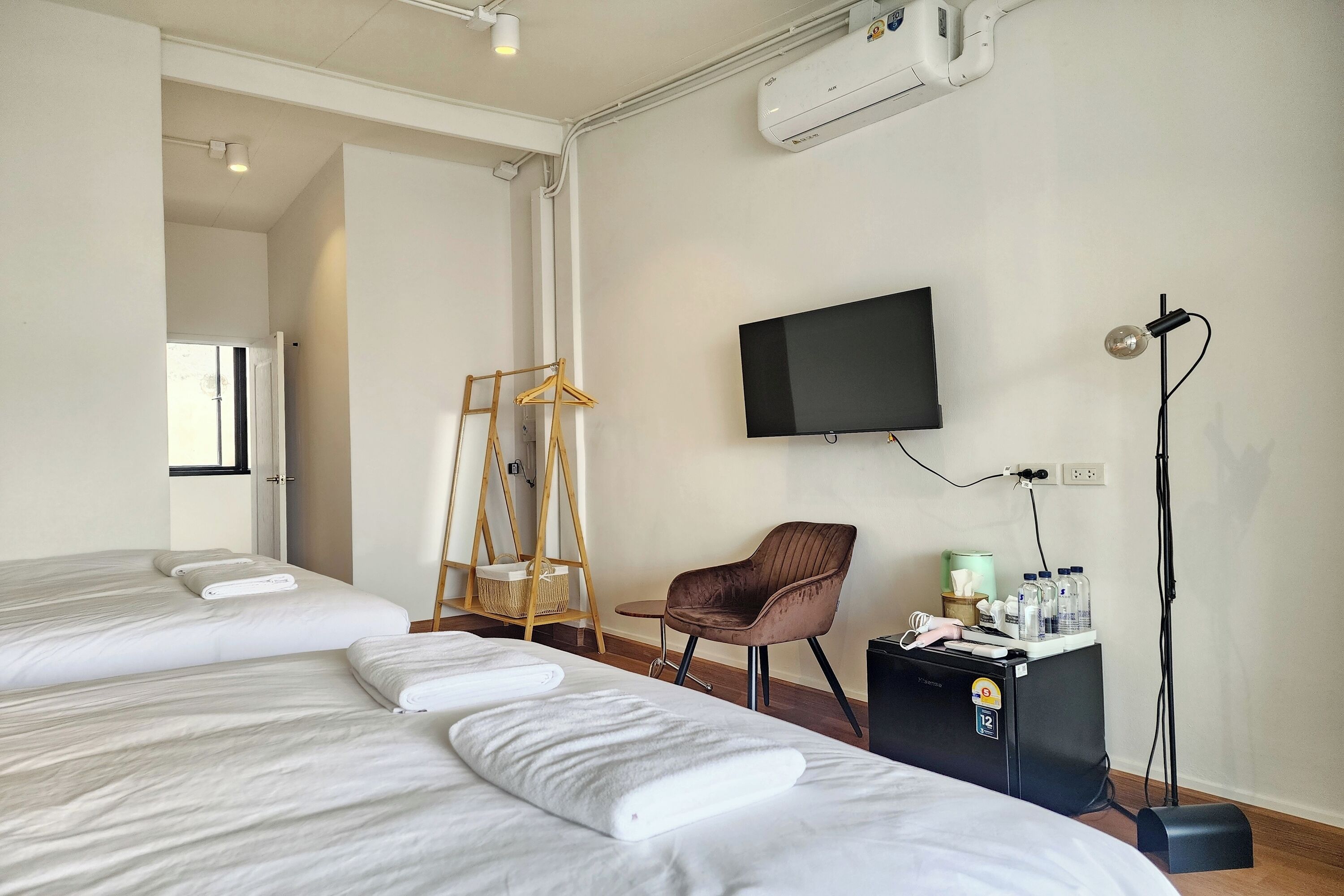 Une chambre d’hôtel avec deux lits, une télévision, une chaise et un bureau équipé d’un ordinateur et de bouteilles.