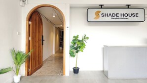 Een receptiegedeelte met een houten deur, een potplant en een bord met de tekst 'SHADE HOUSE Bangkok Oldtown'.
