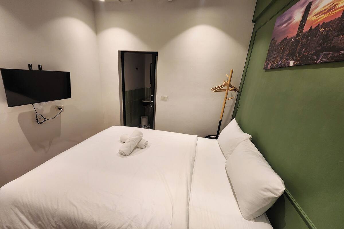 Een hotelkamer met een bed, een flatscreen televisie aan de muur, een groene accentmuur en een stadsgezicht schilderij.
