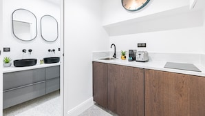 Ein modernes Badezimmer mit einem weißen Waschtisch, zwei schwarzen Waschbecken, einem runden Spiegel, einer Uhr, einer Kaffeemaschine und einem Toaster.