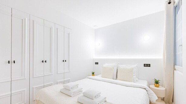 Ein modernes Schlafzimmer mit einem großen Bett, einem weißen Kleiderschrank und einem kleinen Nachttisch mit einer Pflanze.
