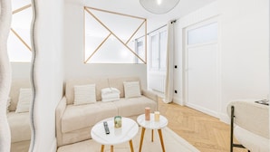 Ein modernes Wohnzimmer mit einem beigen Sofa, zwei weißen runden Tischen und einer geometrischen Wanddekoration.