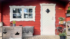 Een rode houten chalet met een witte deur en raam, een klein terras met een bankje, en een bord met de tekst 'FORKEN'.