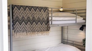 Een slaapkamer met een stapelbed, een deken met een chevrondesign en een kleine lamp.