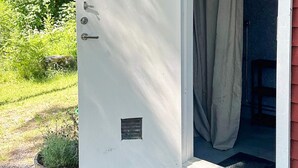 Een witte deur met een klein ventilatierooster en een handgreep, die leidt naar een kamer met een rode gevel en een raam met gordijn.