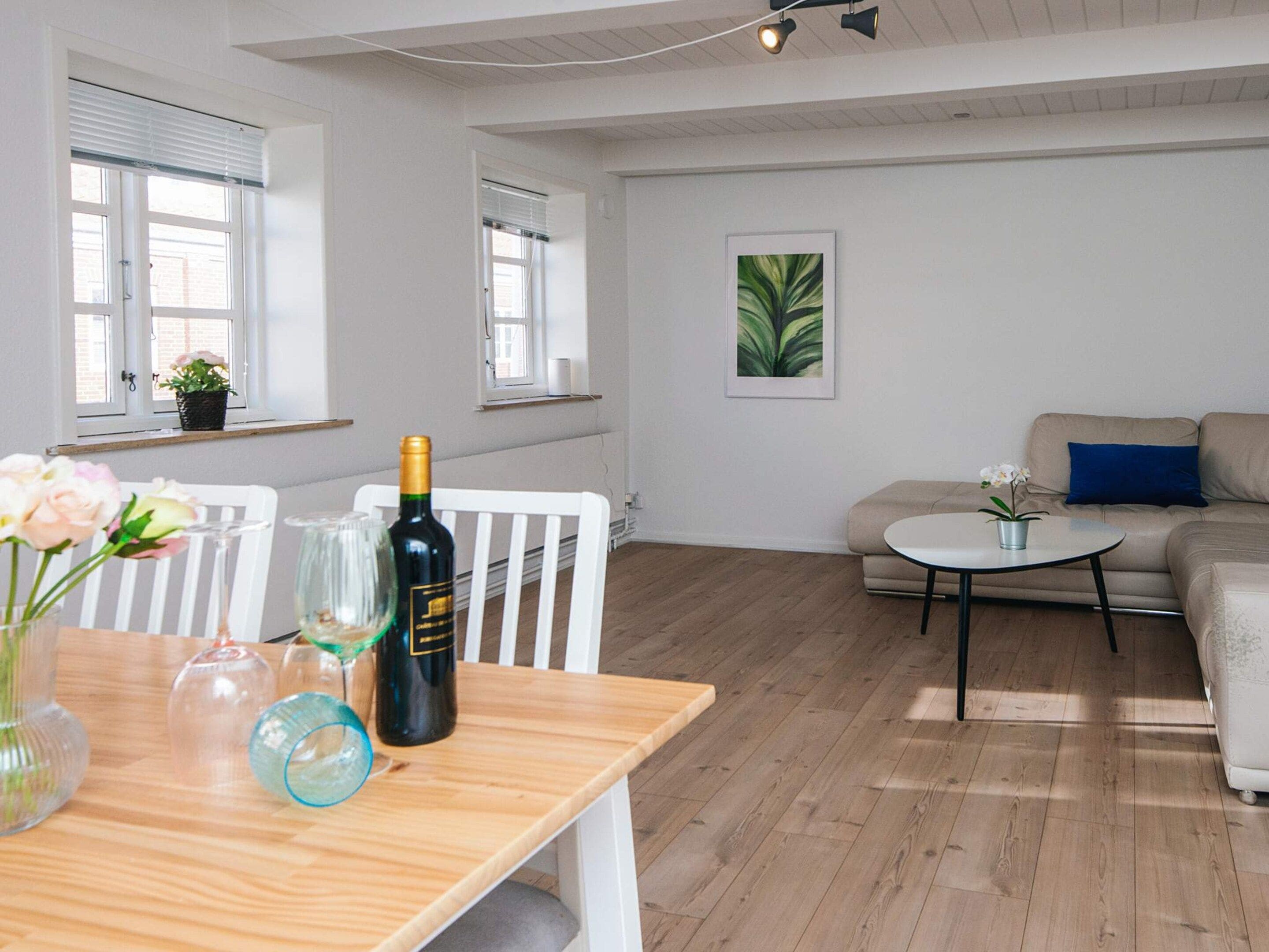 Una sala de estar moderna con una mesa de comedor de madera, un sofá, una pequeña mesa redonda de centro y una planta en maceta.
