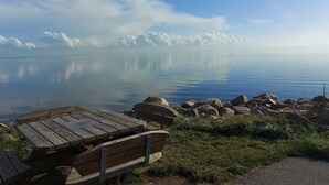 Een kalm meer met een houten bank en picknicktafel op de voorgrond, omringd door rotsen en gras.
