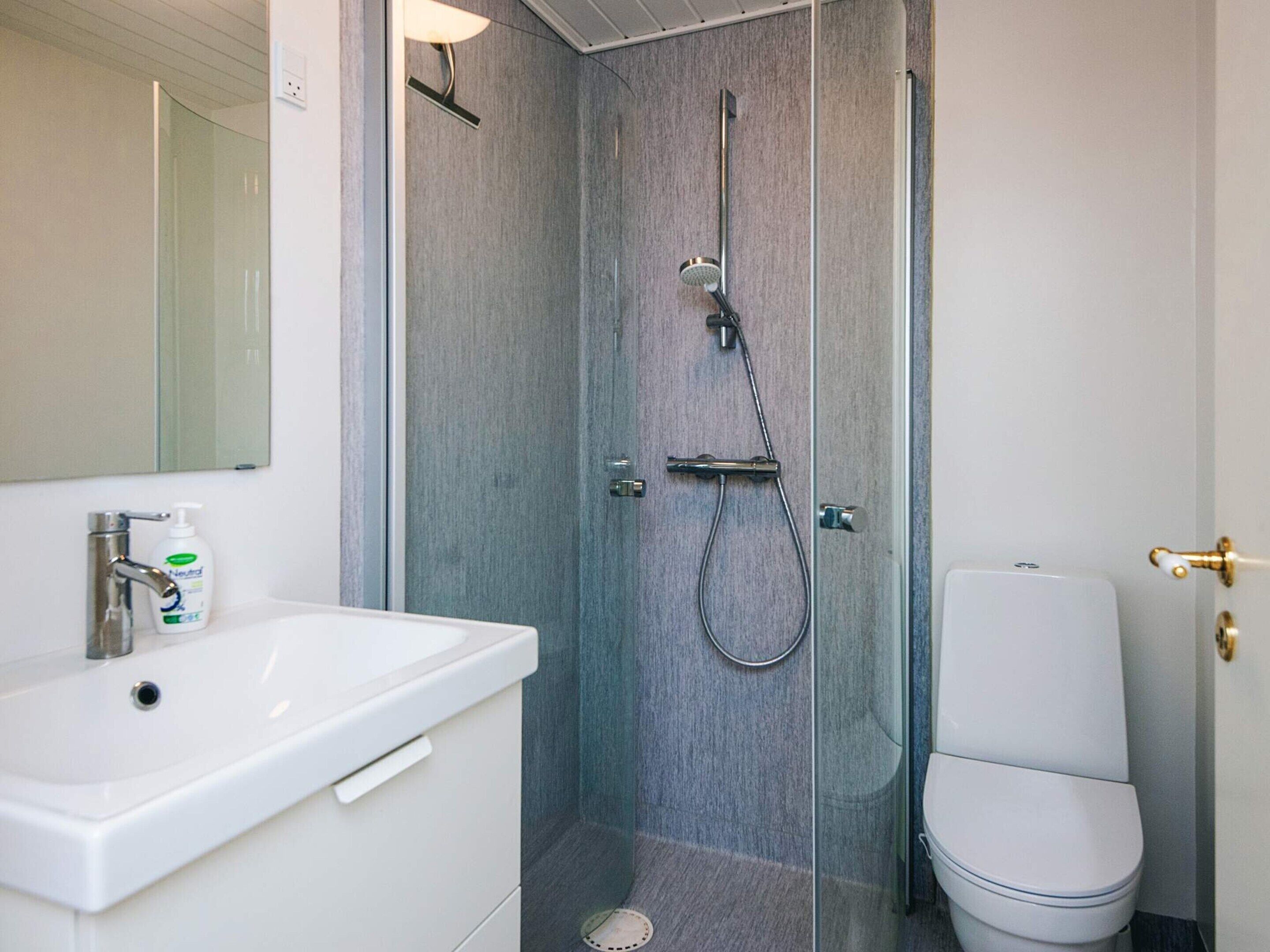 Et badeværelse med bruser, toilet, vask og spejl.