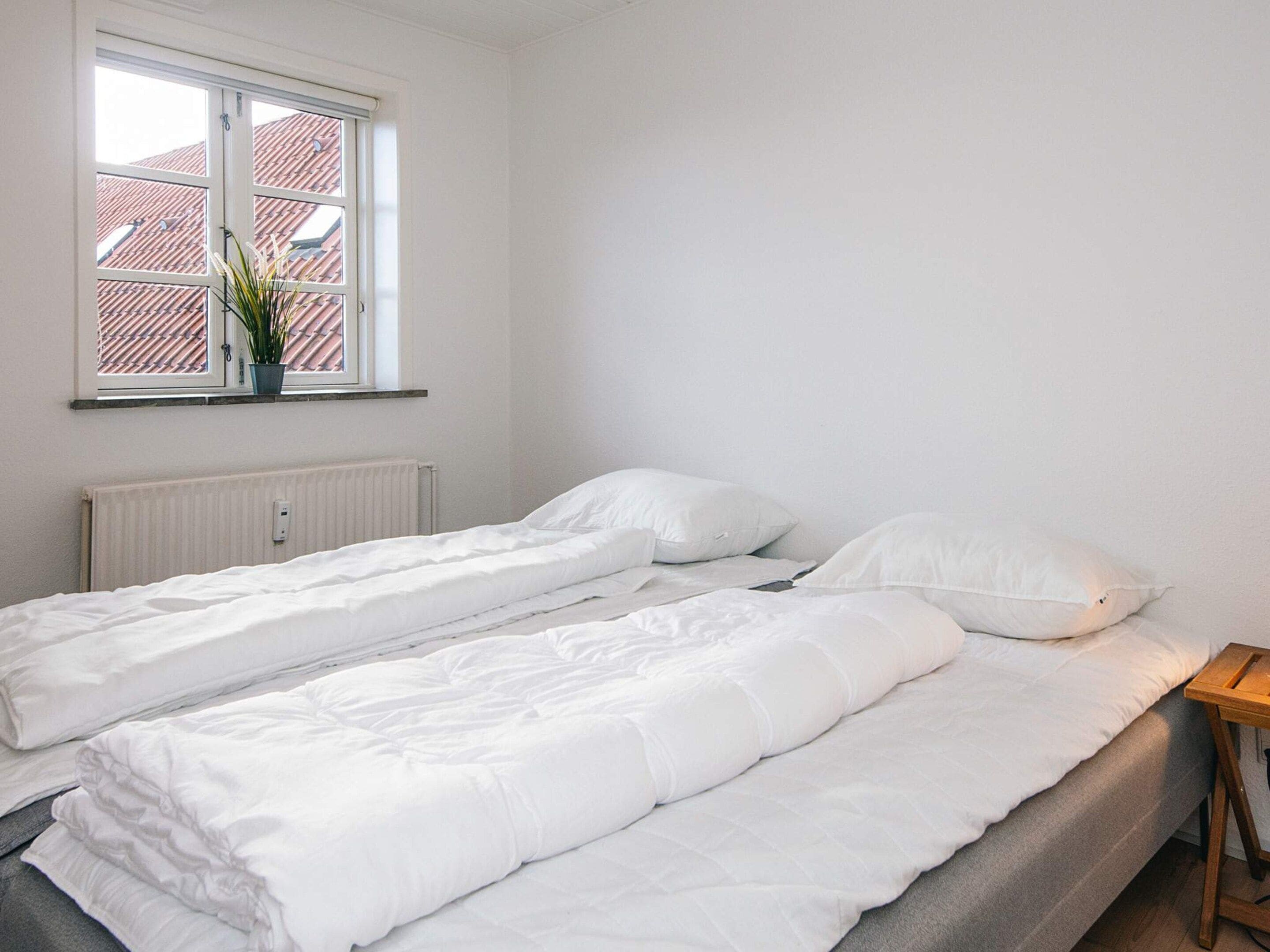 A bedroom with two single beds, a window with a view of a red-roofed building, and a radiator.