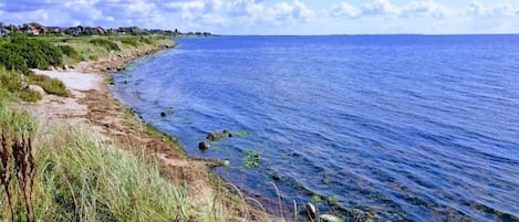 Un paisaje costero con cielo despejado, una playa arenosa y un mar tranquilo.