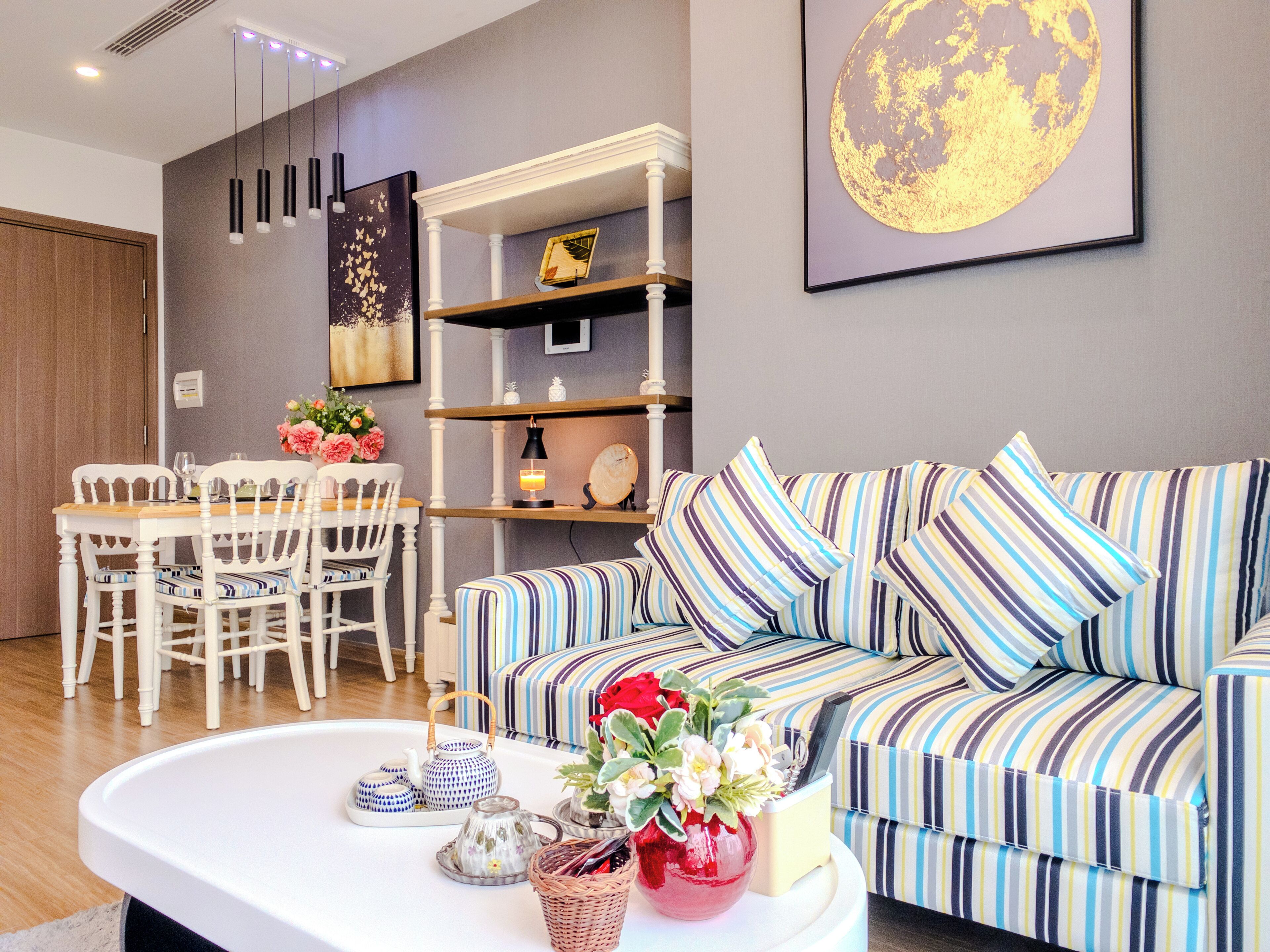 Una sala de estar moderna con un sofá a rayas, una mesa de comedor con sillas, una mesita de centro con adornos y una estantería de pared.