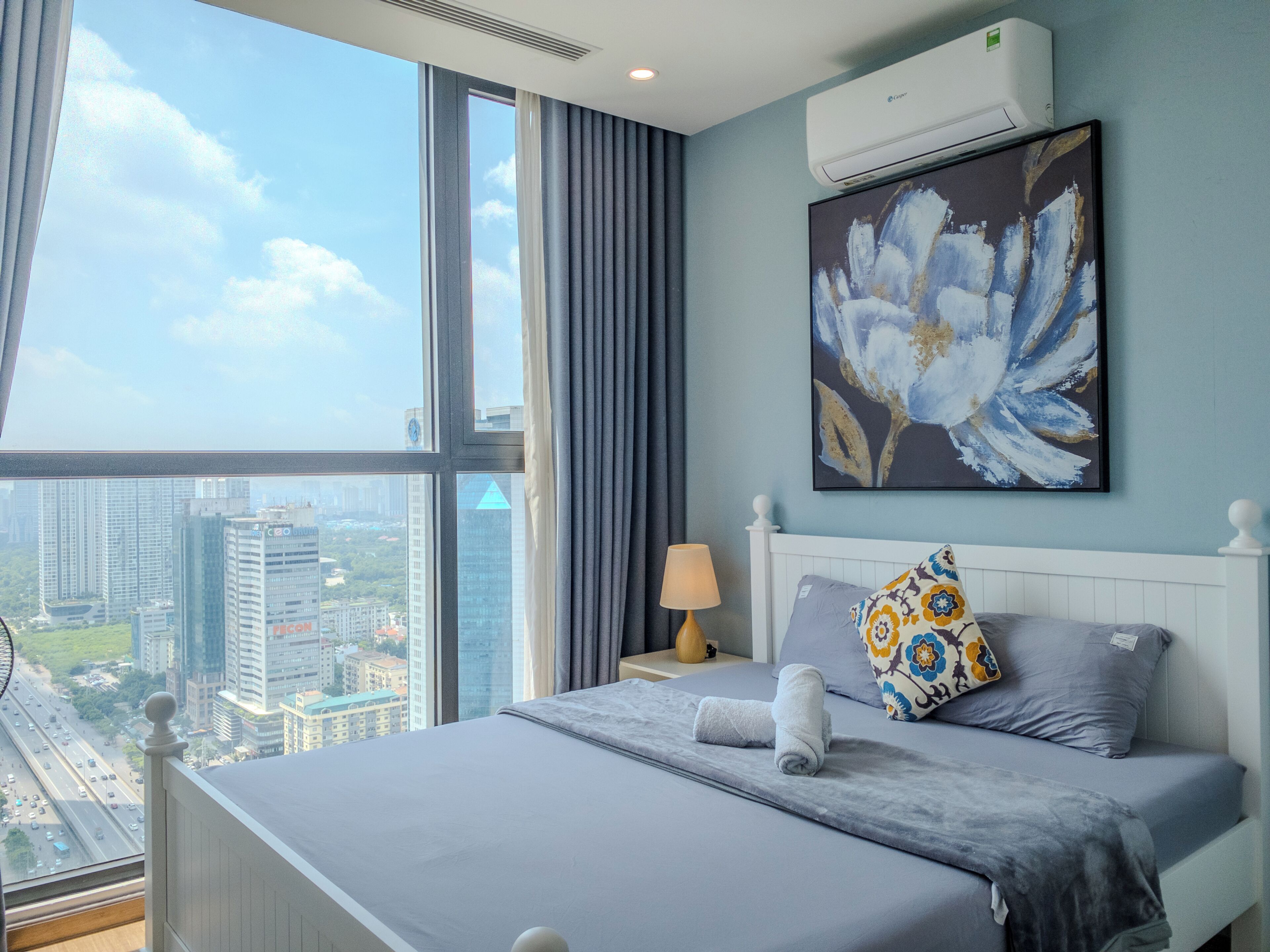 Habitación de hotel moderna con una cama grande, vistas a la ciudad y un equipo de aire acondicionado en la pared.
