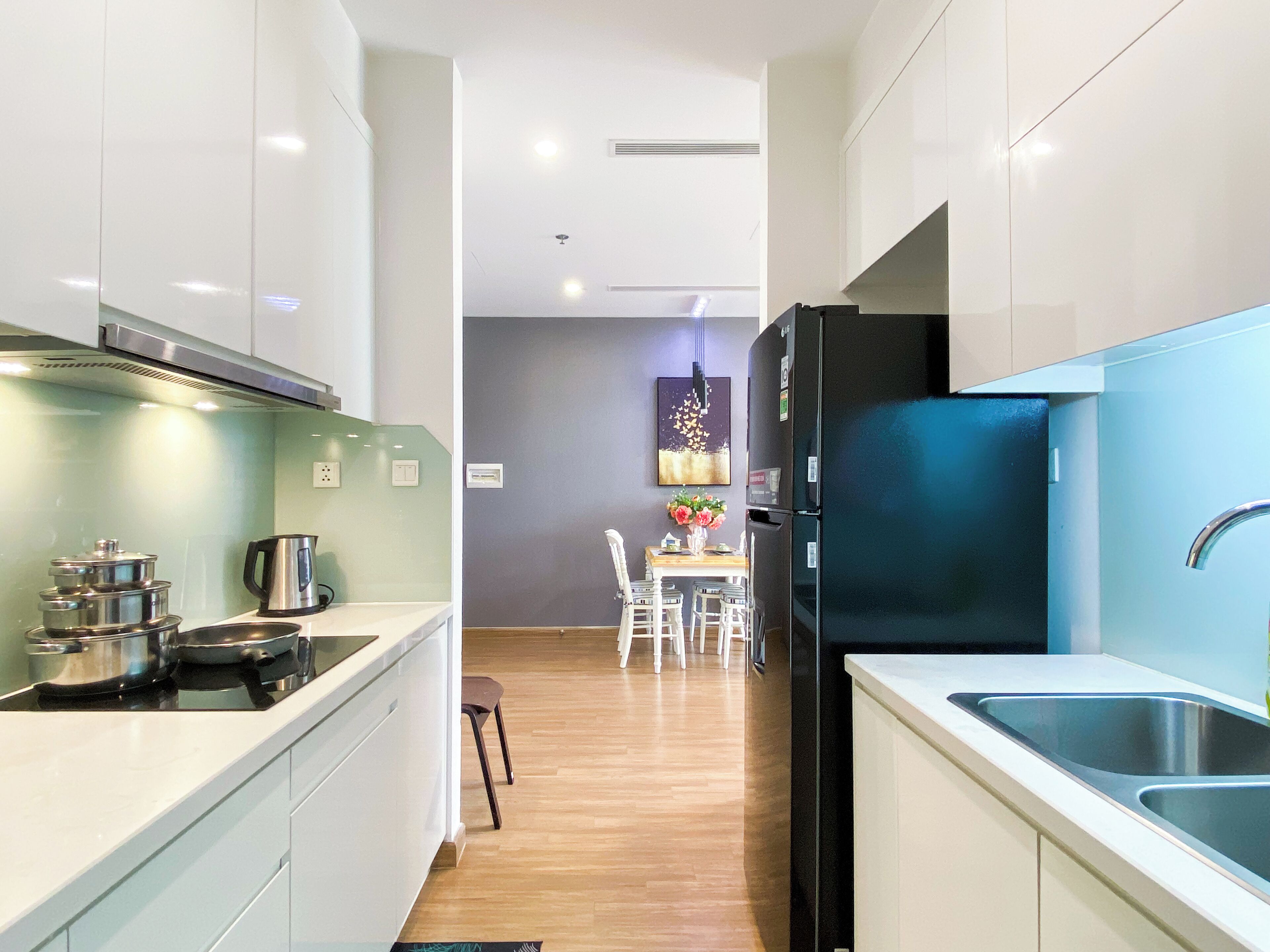 A modern kitchen with white cabinets, a black refrigerator, and a dining area with a table and chairs.