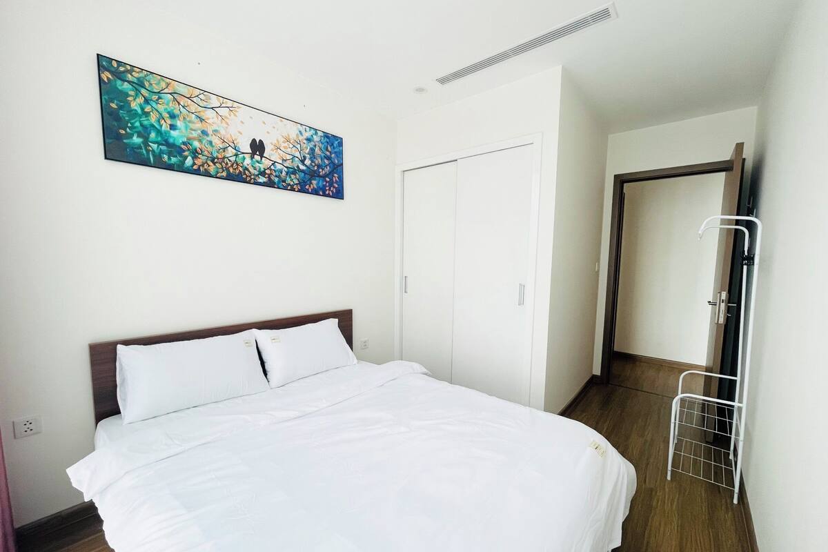 A neatly made bed with white bedding in a room with a wooden floor and white walls. There is a white door and a white radiator on the wall.